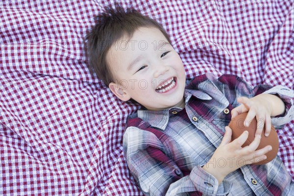 Cute young mixed-race boy playing with football outside on picnic blanket