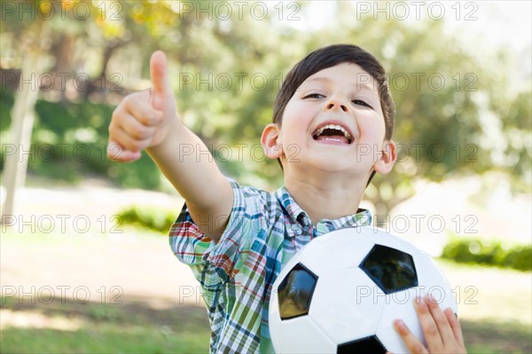 Cute young boy playing with soccer ball and thumbs up outdoors in the park