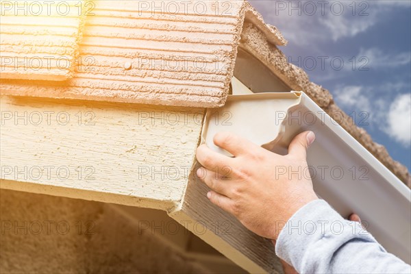 Worker attaching aluminum rain gutter to fascia of house