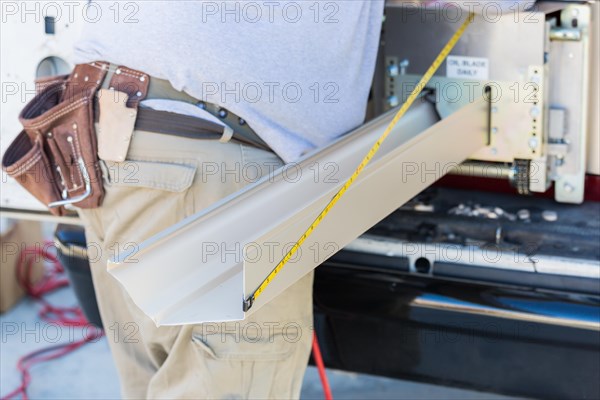 Worker measuring an aluminum rain gutter feeding through seamless shaping machine