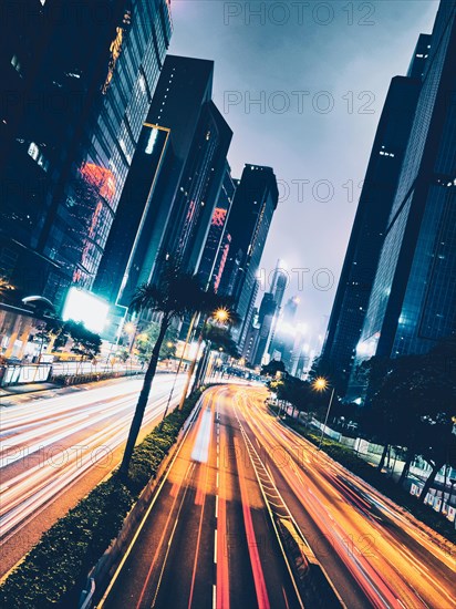 Street traffic in Hong Kong at night. Office skyscraper buildings and busy traffic on highway road with blurred cars light trails. Hong Kong