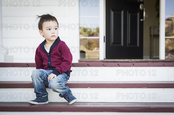 Cute melancholy mixed-race boy sitting on front porch steps