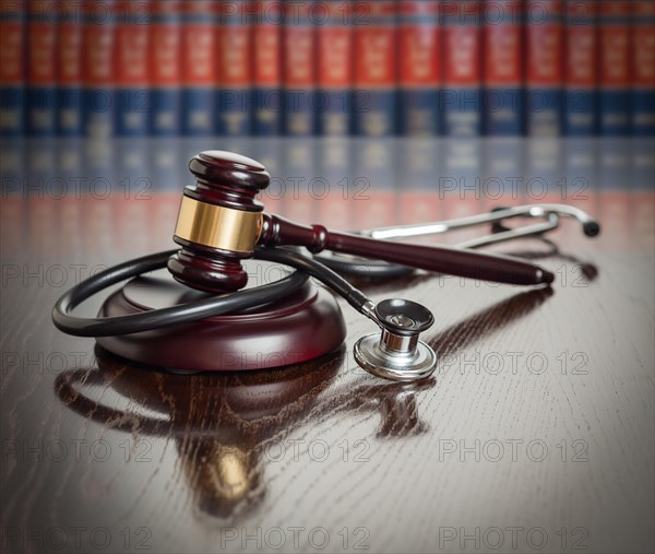 Gavel and stethoscope on wooden table with law books in background