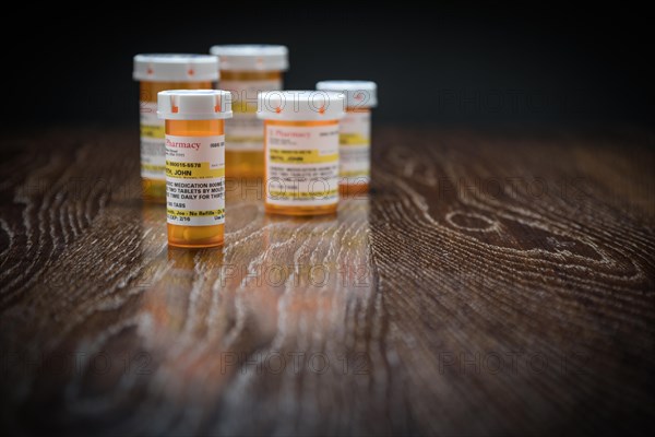 Variety of non-proprietary prescription medicine bottles on reflective wooden surface