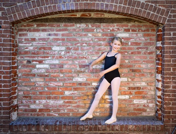 Cute caucasian ballerina girl posting against A brick wall