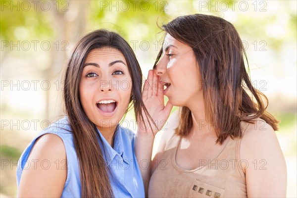 Two beautiful ethnic twin sisters whispering secrets outdoors