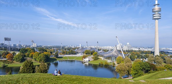 Two people sitting in the park with Olympic lake and Olympic tower