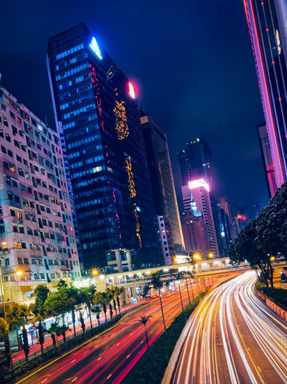 Street traffic in Hong Kong at night. Office skyscraper buildings and busy traffic on highway road with blurred cars light trails. Hong Kong