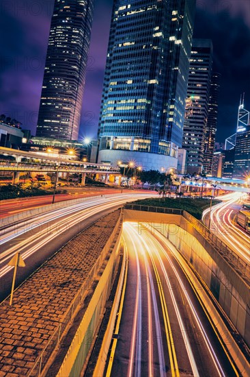 Street traffic in Hong Kong at night. Office skyscraper buildings and busy traffic on highway road with blurred cars light trails. Hong Kong