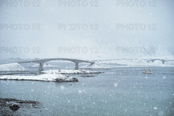 Fredvang bridges in heavy snowfall in winter with fishing ship. Lofoten islands