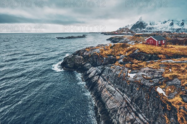 Clif with traditional red rorbu house on Litl-Toppoya islet on Lofoten Islands