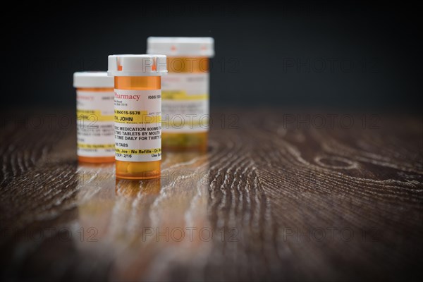 Variety of non-proprietary prescription medicine bottles on reflective wooden surface