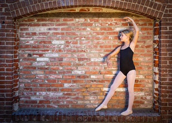 Cute caucasian ballerina girl posting against A brick wall