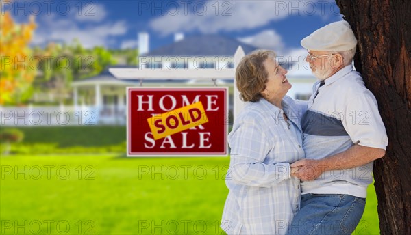 Sold real estate sign with happy affectionate senior couple hugging in front of house