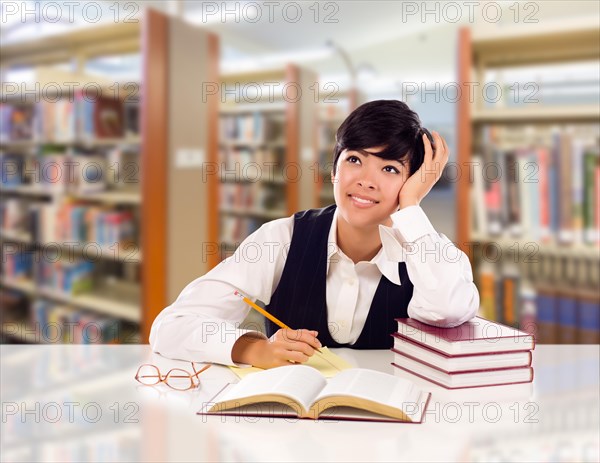 Young female mixed-race student with books and paper daydreaming in library looking to the left