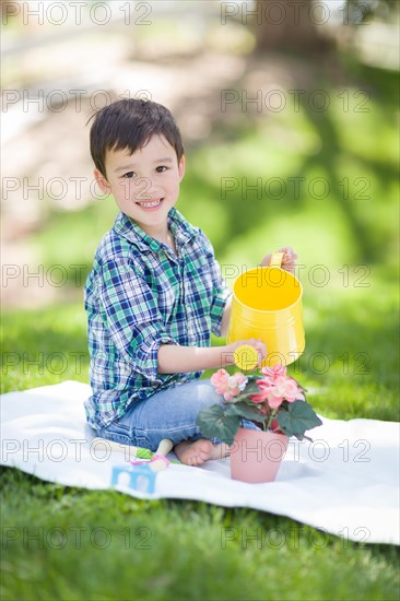 mixed-race young boy watering his potted flowers outside on the grass