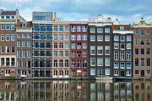 Row of typical houses and boat on Amsterdam canal Damrak with reflection. Amsterdam