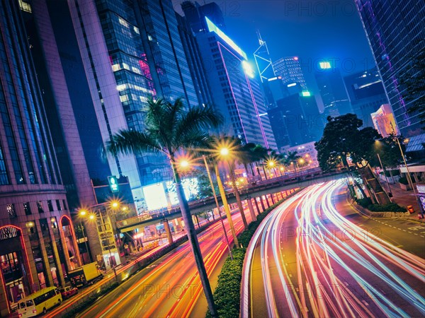 Street traffic in Hong Kong at night. Office skyscraper buildings and busy traffic on highway road with blurred cars light trails. Hong Kong