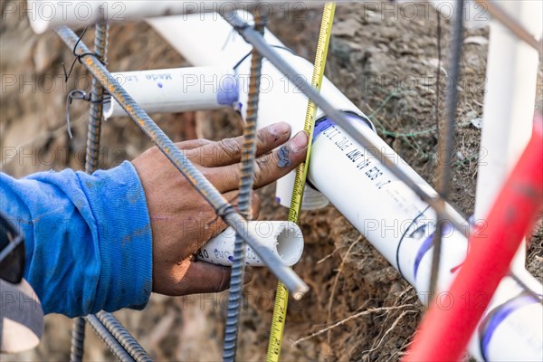 Plumber using tape measure while installing PVC pipe at construction site