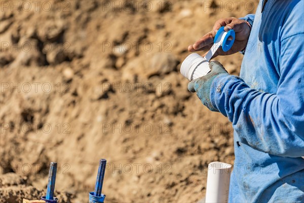 Plumber applying PTFE tape to PVC pipe at construction site