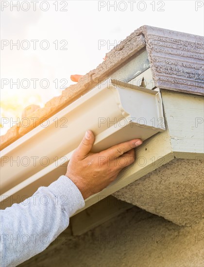 Worker attaching aluminum rain gutter to fascia of house