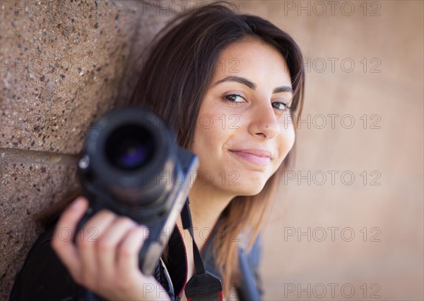 Young adult ethnic female photographer against wall holding camera