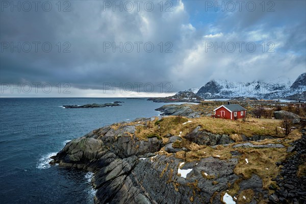 Clif with traditional red rorbu house on Litl-Toppoya islet on Lofoten Islands