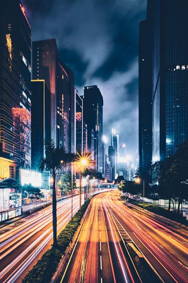 Street traffic in Hong Kong at night. Office skyscraper buildings and busy traffic on highway road with blurred cars light trails. Hong Kong