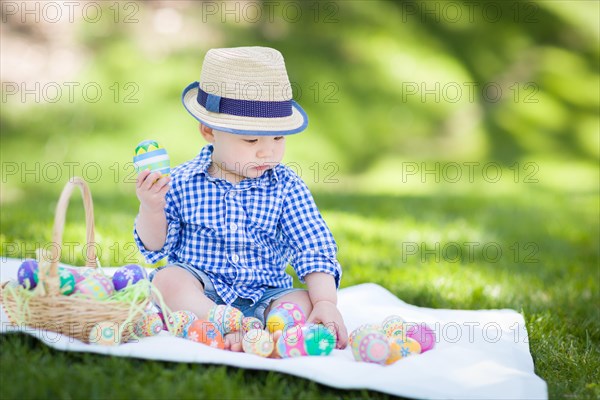 mixed-race chinese and caucasian baby boy outside wearing rabbit ears playing with easter eggs