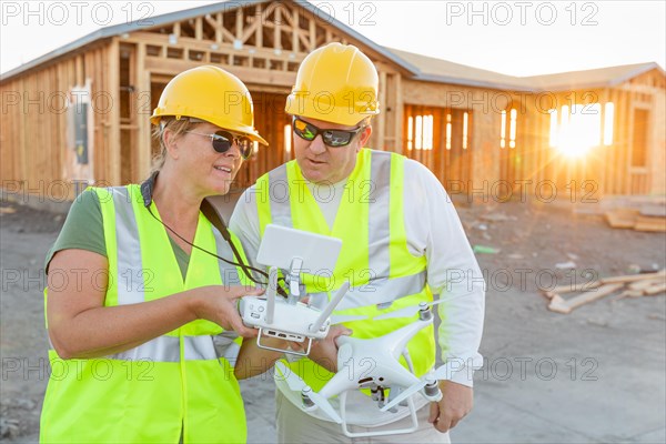 Workers with drone quadcopter inspecting photographs on controller at contruction site