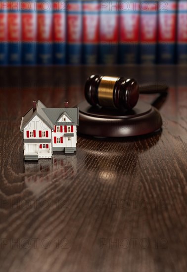 Gavel and small model house on wooden table with law books in background