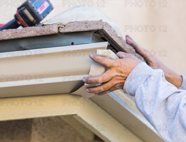 Worker attaching aluminum rain gutter to fascia of house