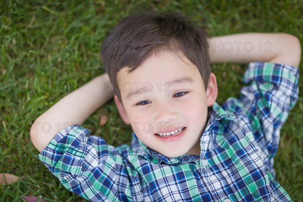 Thoughtful mixed-race chinese and caucasian young boy relaxing on his back outside on the grass