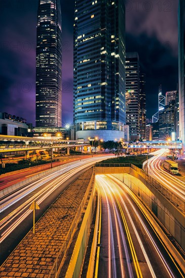 Street traffic in Hong Kong at night. Office skyscraper buildings and busy traffic on highway road with blurred cars light trails. Hong Kong