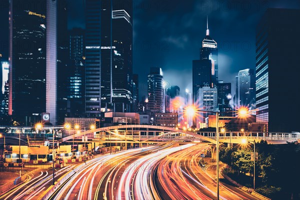 Street traffic in Hong Kong at night. Office skyscraper buildings and busy traffic on highway road with blurred cars light trails. Hong Kong