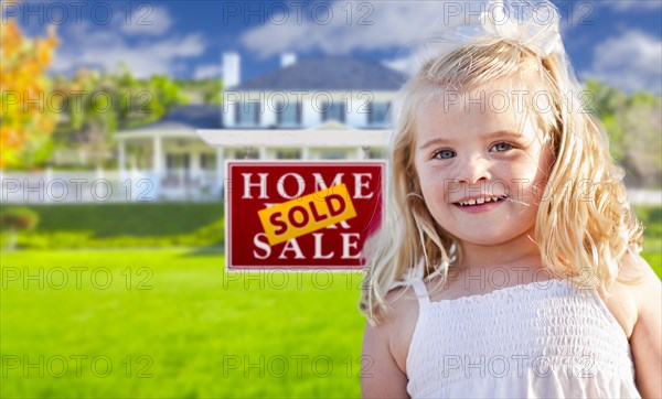 Cute smiling girl in front yard with sold for sale real estate sign and house