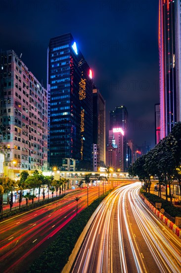 Street traffic in Hong Kong at night. Office skyscraper buildings and busy traffic on highway road with blurred cars light trails. Hong Kong