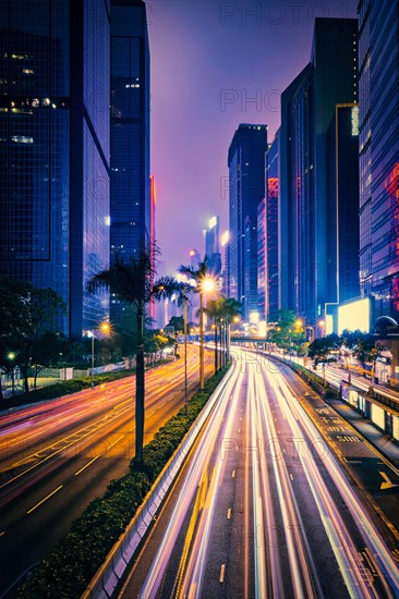 Street traffic in Hong Kong at night. Office skyscraper buildings and busy traffic on highway road with blurred cars light trails. Hong Kong