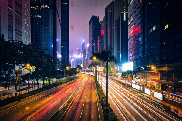 Street traffic in Hong Kong at night. Office skyscraper buildings and busy traffic on highway road with blurred cars light trails. Hong Kong