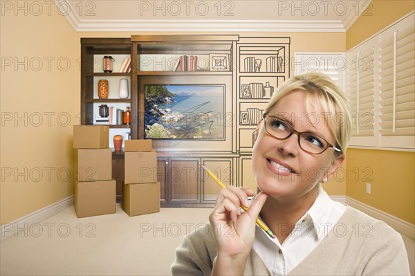 Female holding pencil in room with moving boxes and drawing of entertainment unit on wall