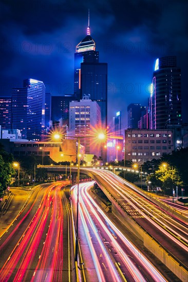 Street traffic in Hong Kong at night. Office skyscraper buildings and busy traffic on highway road with blurred cars light trails. Hong Kong