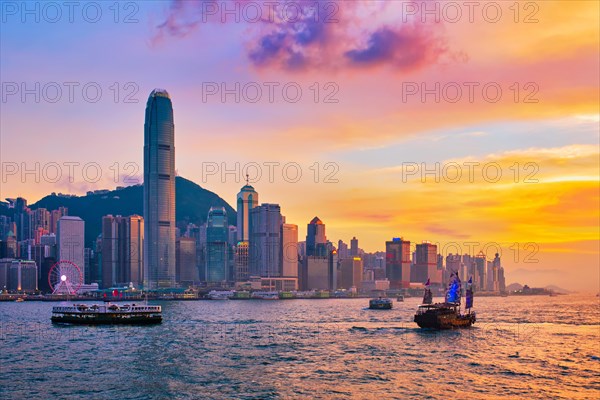 Hong Kong skyline cityscape downtown skyscrapers over Victoria Harbour in the evening with ferry boat and junk boat on sunset. Hong Kong
