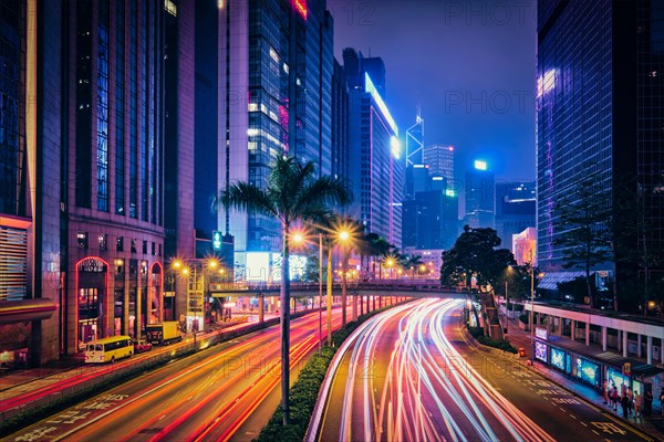 Street traffic in Hong Kong at night. Office skyscraper buildings and busy traffic on highway road with blurred cars light trails. Hong Kong