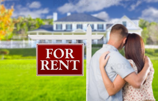 For rent real estate sign and affectionate military couple looking at nice new house