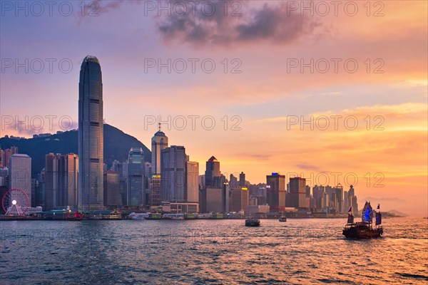 Hong Kong skyline cityscape downtown skyscrapers over Victoria Harbour in the evening with junk tourist ferry boat on sunset with dramatic sky. Hong Kong