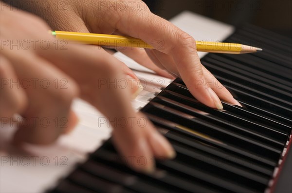 Woman's fingers with pencil on digital piano keys