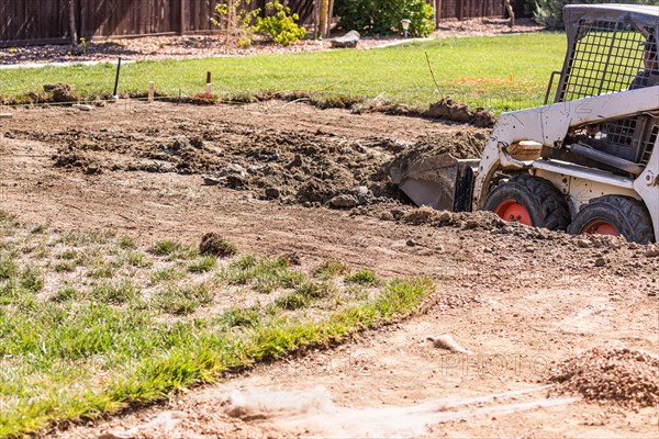 Small bulldozer digging in yard for pool installation