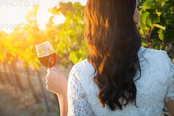 Young adult woman enjoying glass of wine tasting walking in the vineyard