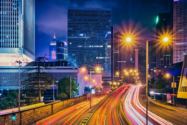 Street traffic in Hong Kong at night. Office skyscraper buildings and busy traffic on highway road with blurred cars light trails. Hong Kong