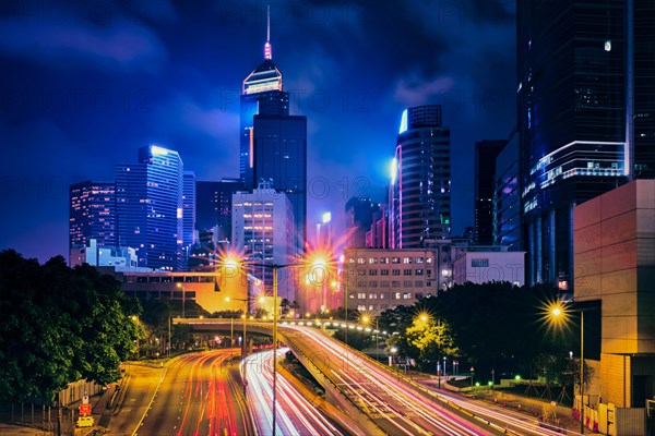 Street traffic in Hong Kong at night. Office skyscraper buildings and busy traffic on highway road with blurred cars light trails. Hong Kong